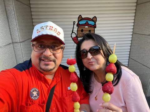       Two people enjoying fruit skewers in front of a shop.
  