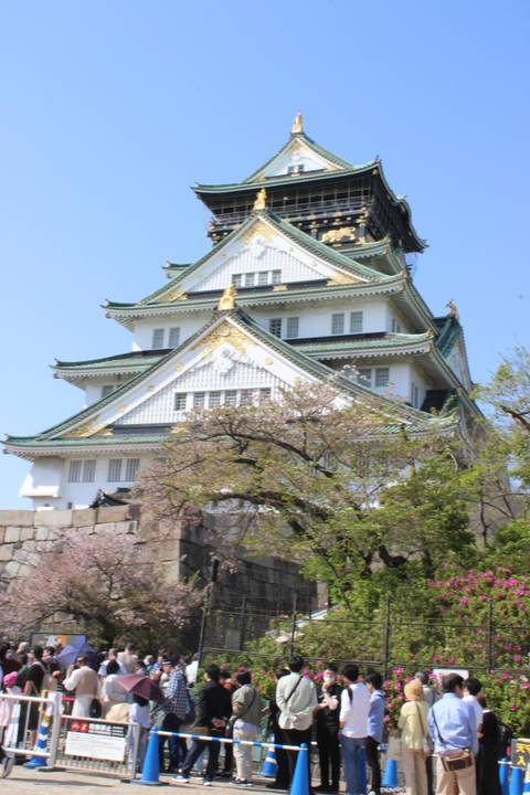       A bustling scene in front of Osaka Castle with cherry blossoms.
  