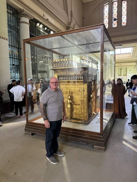       Man posing in front of a golden exhibit inside a museum.
  