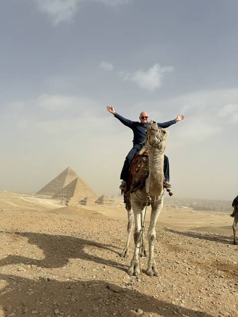       Person on a camel with pyramids in the background.
  