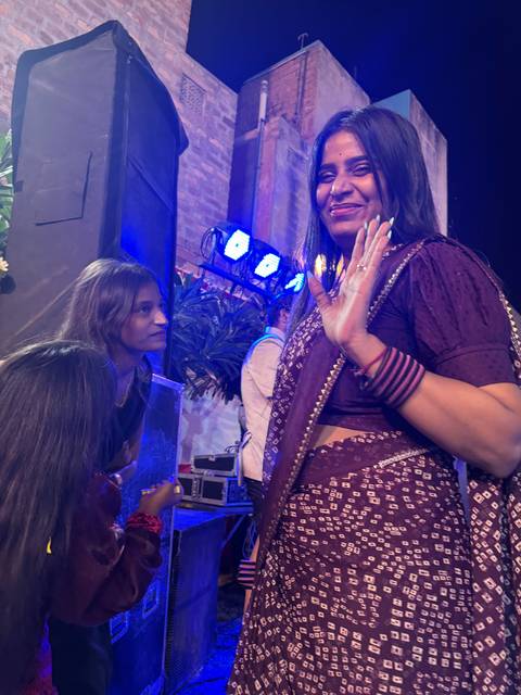       Woman in traditional attire waving at a nighttime event.
  