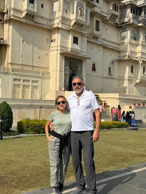       Couple posing in front of a large building in a park.
  