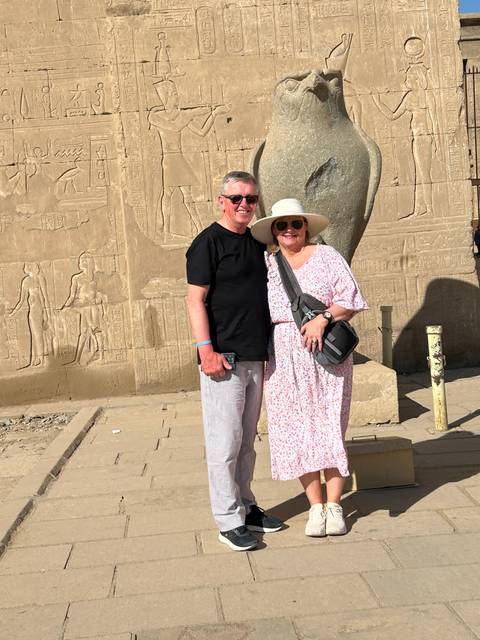 Two people posing in front of an ancient stone statue with hieroglyphics.