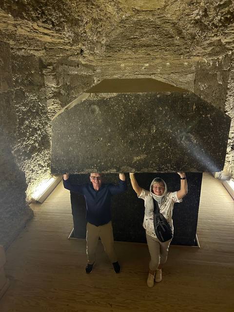       Two people standing beside a large stone slab in a dimly lit space.
  