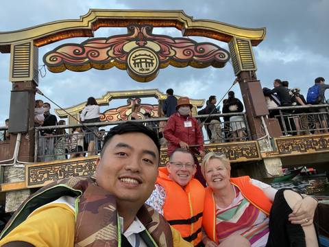       People posing under a decorated arch with a crowd in the background.
  