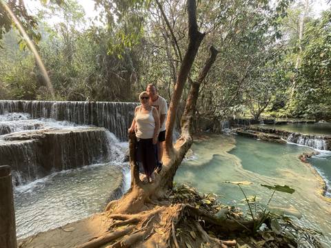      Two people standing beside waterfalls surrounded by lush vegetation.
  