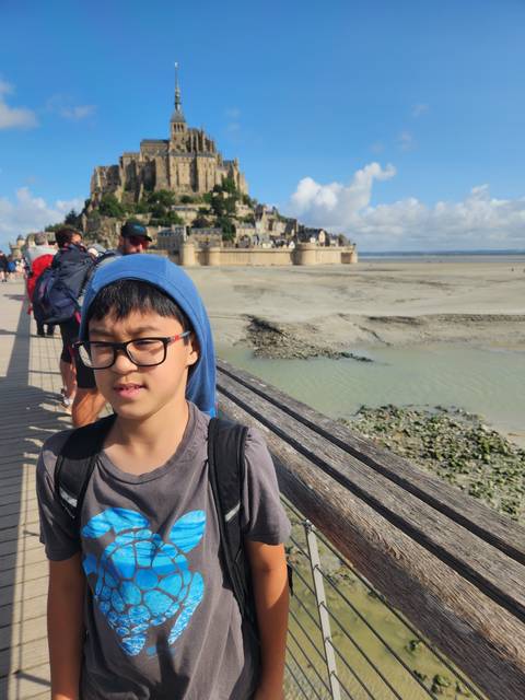 Child standing on a bridge with a scenic old town in the background.