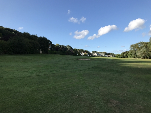 An open golf course with trees and a few houses in the distance.