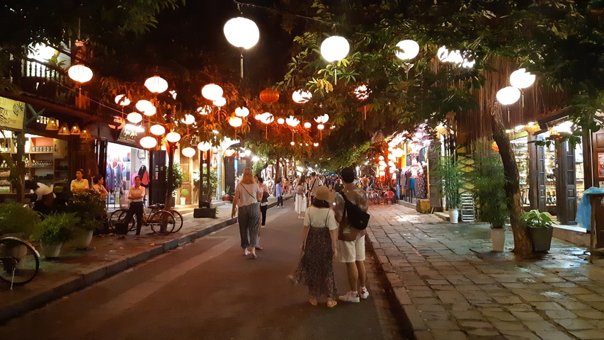       Illuminated street with lanterns and people walking.
  