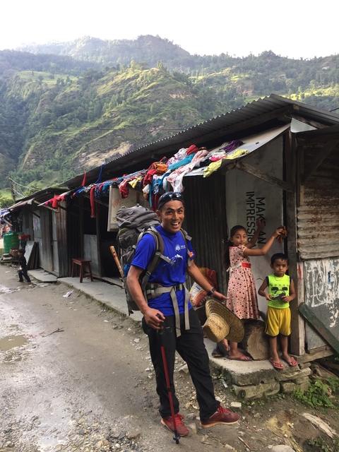A person with a backpack smiling, with a child and laundry in the background.