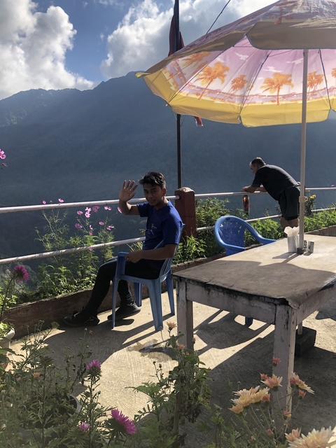 A person sitting on a chair on a balcony overlooking a hilly landscape.