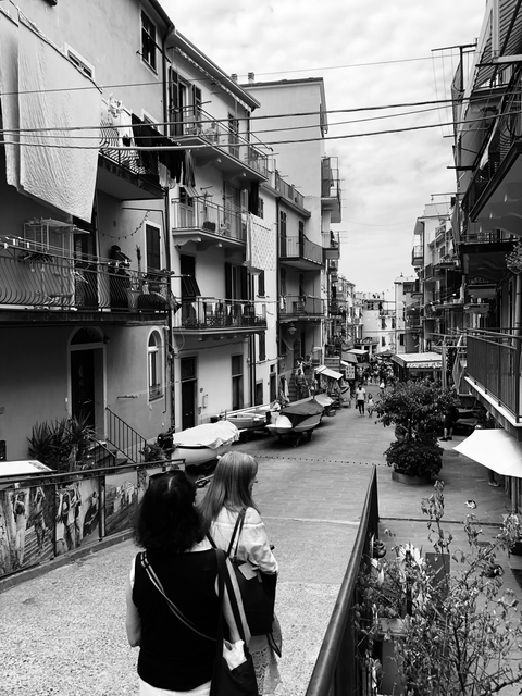       Busy street with boats and people in a coastal town.
  