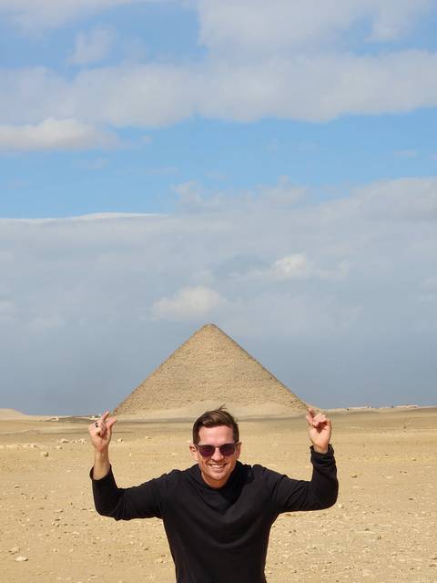 Man posing with the pyramid in the background.