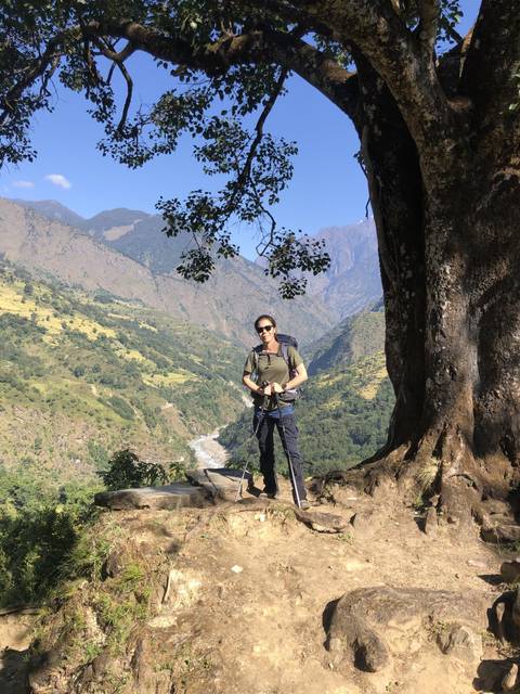 Hiker posing near a tree with mountain backdrop.