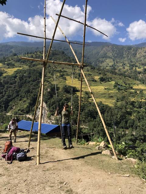 Person posing near wooden frame structure with scenic mountains.