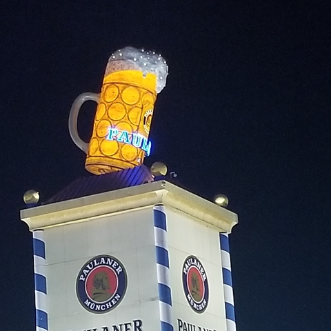 Illuminated beer mug glass atop a building at night.