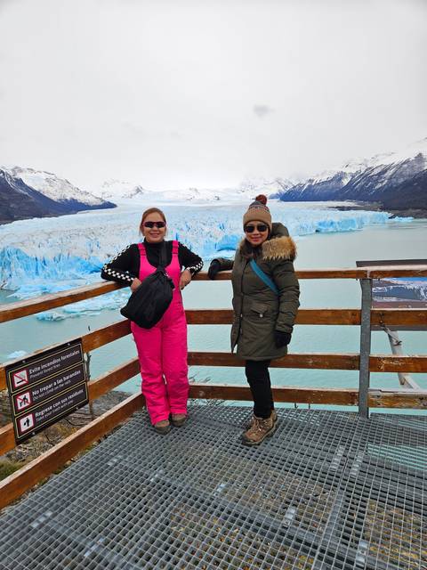 Two women standing on a viewpoint deck overlooking a glacier.
