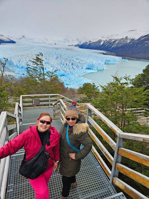 Two women on a metal deck with views of a glacier and mountains.
