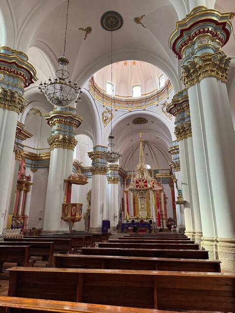       Ornate interior of a grand cathedral with chandeliers and gold detailing.
  
