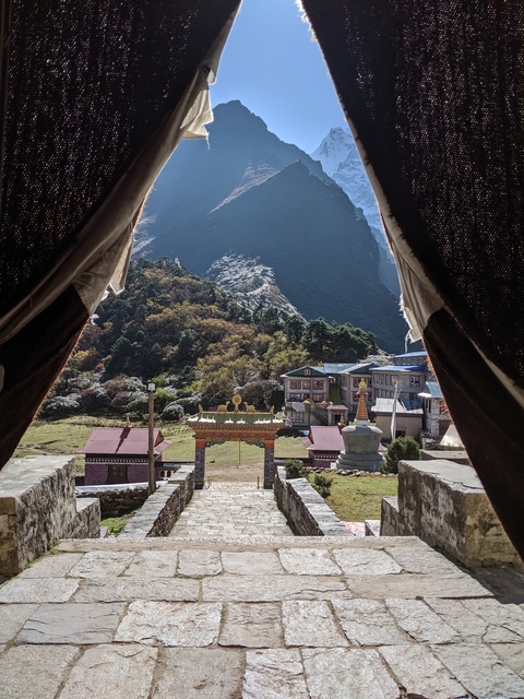 View from a stone archway to a monastery with mountains in the backdrop.