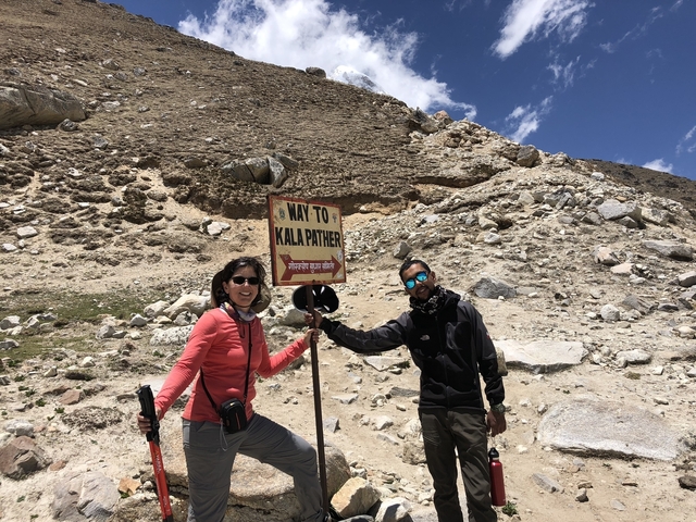 Two people posing by a sign pointing to Kala Patthar.