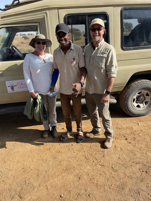 Three people posing next to a safari vehicle.