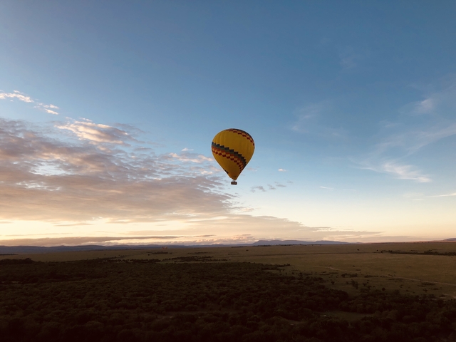 Hot air balloon floating over a scenic plain at sunset.
