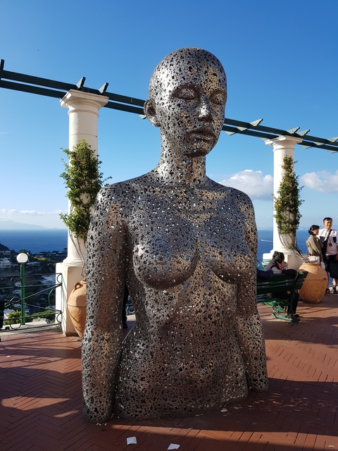       Sculpture of a torso made of small metallic pieces with a seascape in the background.
  