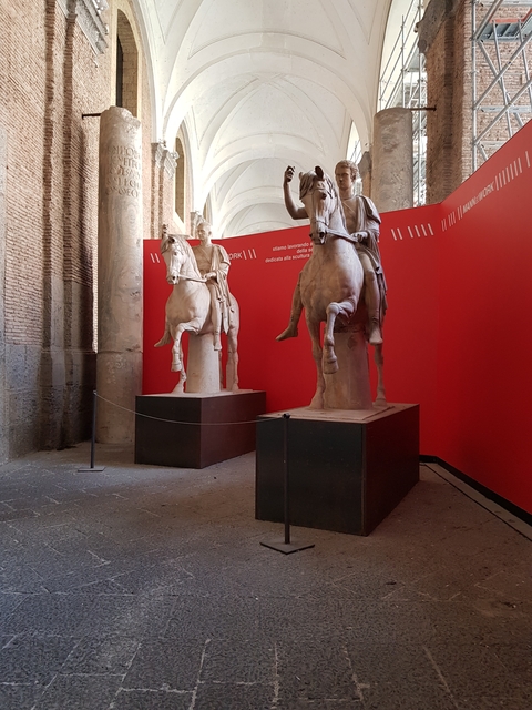       Statues of horse-mounted riders with a red backdrop in a museum.
  