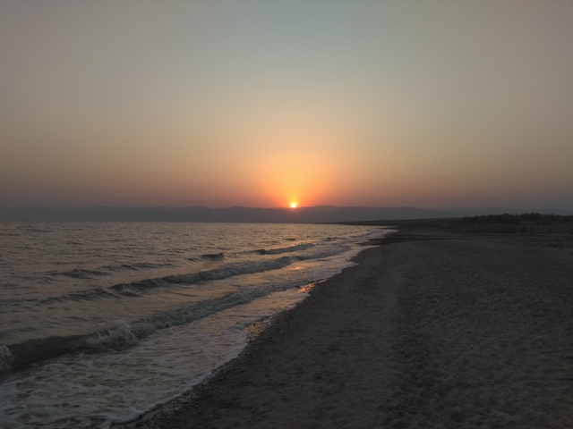      Sunset over a calm beach shoreline.
  