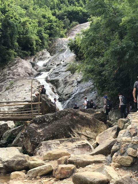       People hiking near a waterfall in a rocky terrain.
  