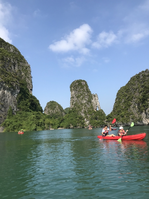       Kayakers paddling in a turquoise bay surrounded by limestone karsts.
  
