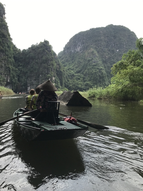       People rowing boats surrounded by lush green cliffs.
  
