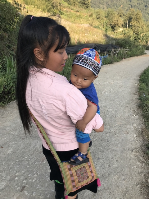       A person holding a baby against a natural backdrop.
  
