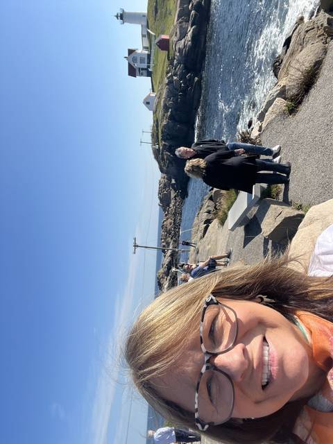 Woman smiling with the ocean and rocks in the background.