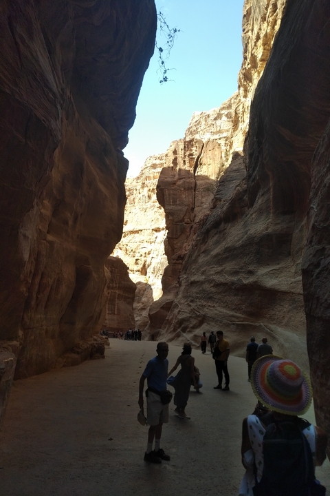 Narrow pathway through towering rocky cliffs with people walking.