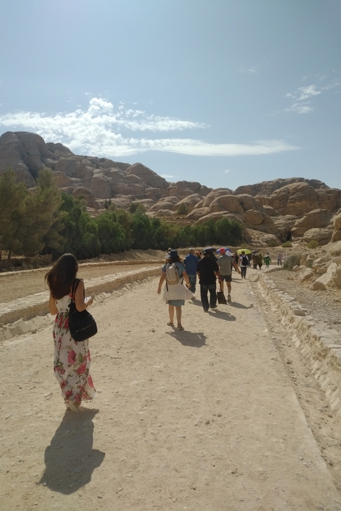 Tourists walking through a path surrounded by rocky terrain and trees.