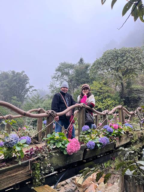       Two people posing on a flower-decorated bridge.
  