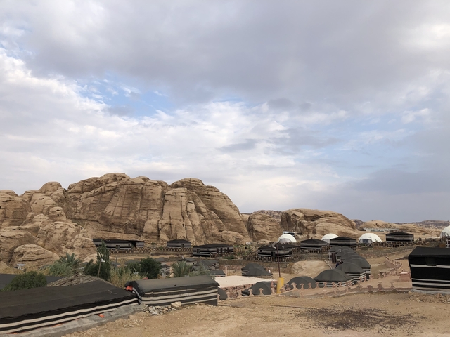 Desert landscape with tents and rocky hills under a cloudy sky.
