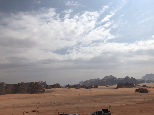 Vast desert landscape with mountains in the distance under a cloudy sky.