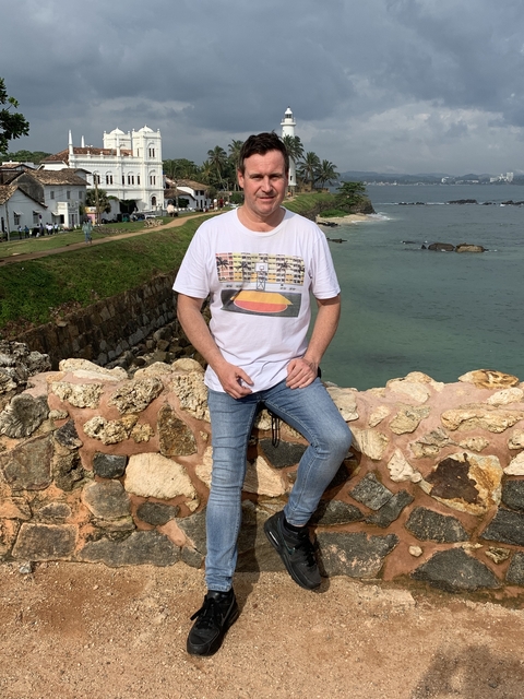 Man posing on a stone wall by the sea.