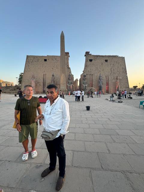       Two men standing in front of an ancient structure with a tall obelisk.
  