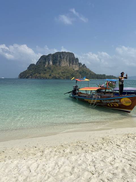 Longtail boats anchored along a tropical beach with clear water.
