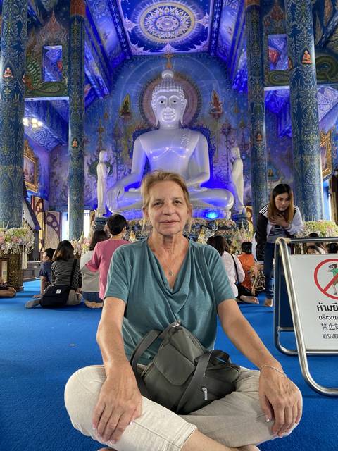 Woman sitting in front of a large white Buddha statue inside a temple.