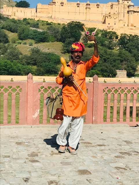       Man in traditional attire holding a gourd bottle and gesturing.
  