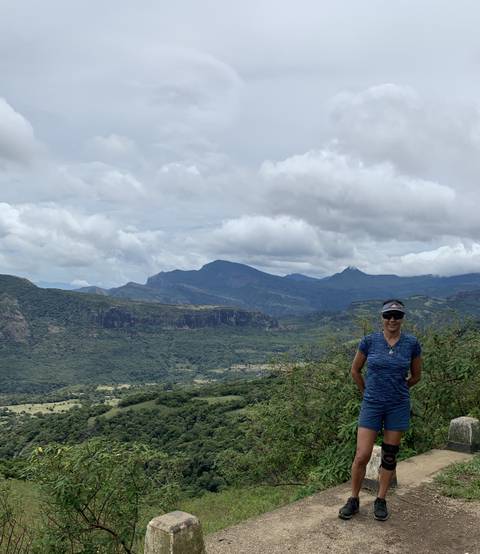       A person standing in a mountainous area with clouds in the background.
  