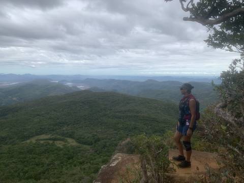       A person standing at the edge of a cliff overlooking green hills and a cloudy sky.
  