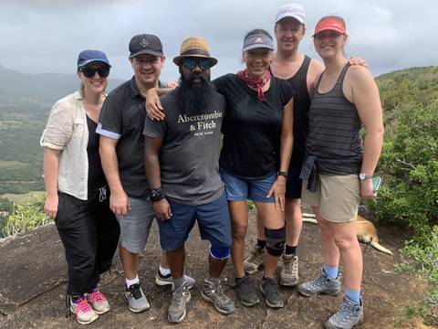       A group of six people posing on a hillside wearing casual hiking attire.
  