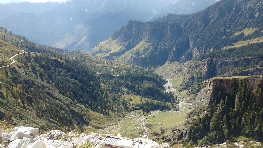 Panoramic view of a deep valley with roads and trees, mountains in the background.