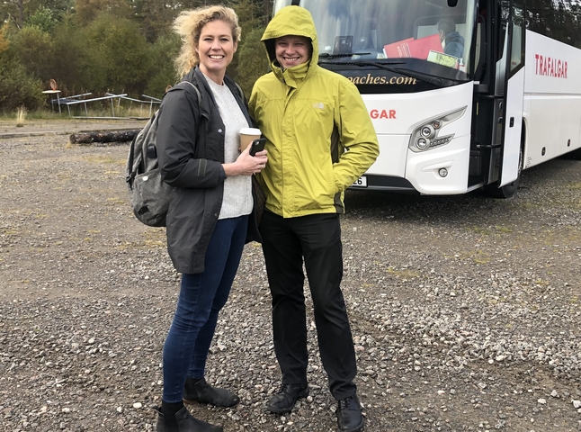       Two people standing in front of a tour bus.
  